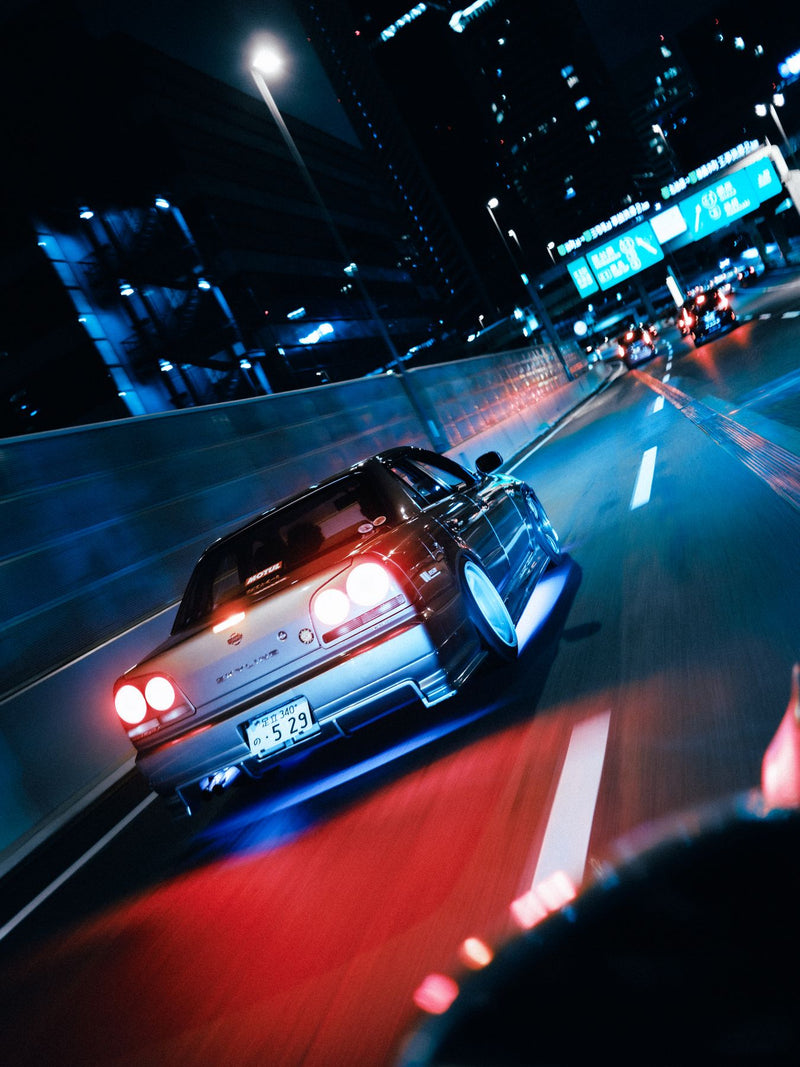 Car following another through neon-lit streets at night