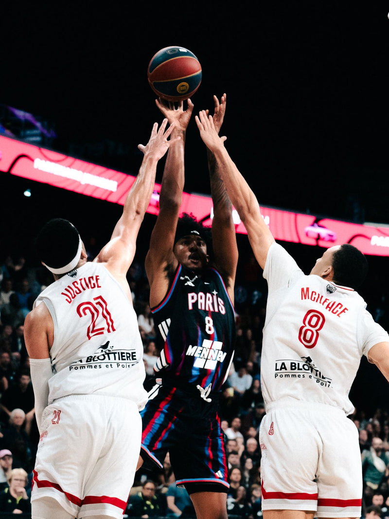 Contested jump shot between three players under the lights