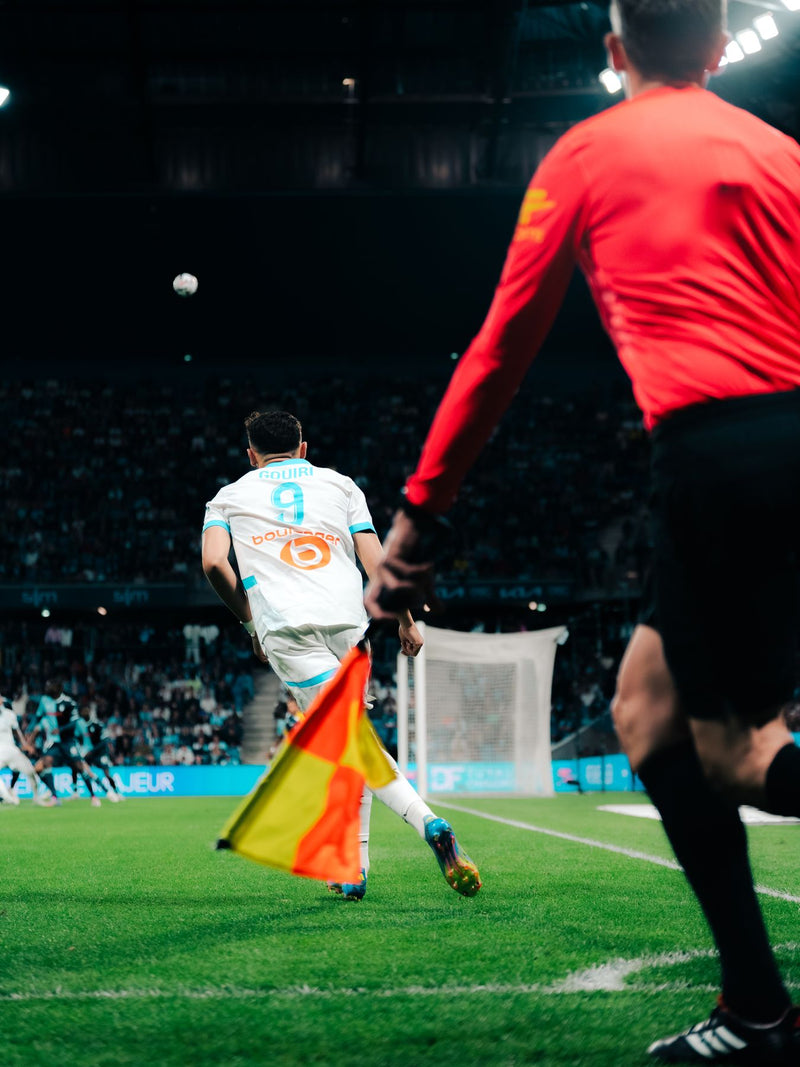 Corner kick being taken beside the corner flag, assistant referee in the foreground