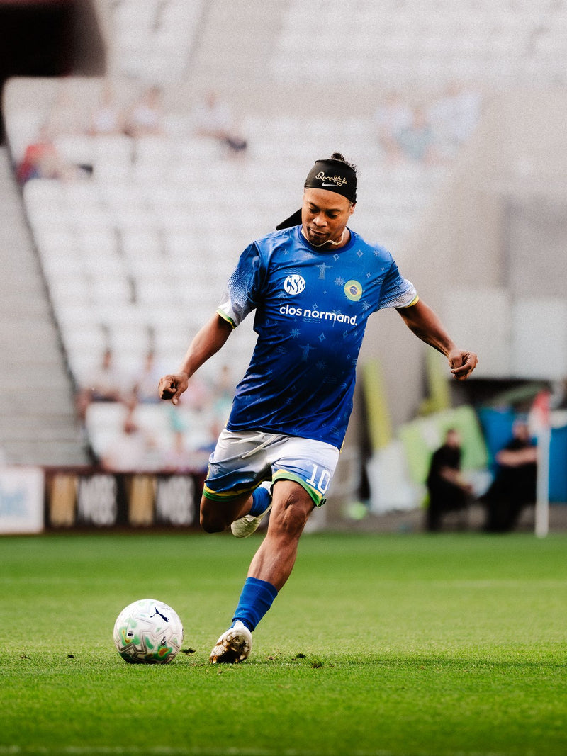 Player in a blue kit striking the ball on an empty stadium pitch