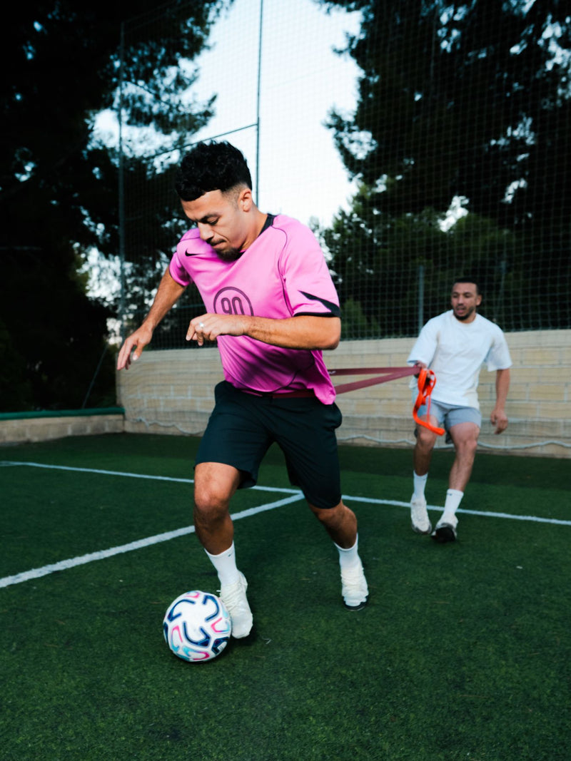 Player in a pink shirt controlling the ball on an outdoor pitch