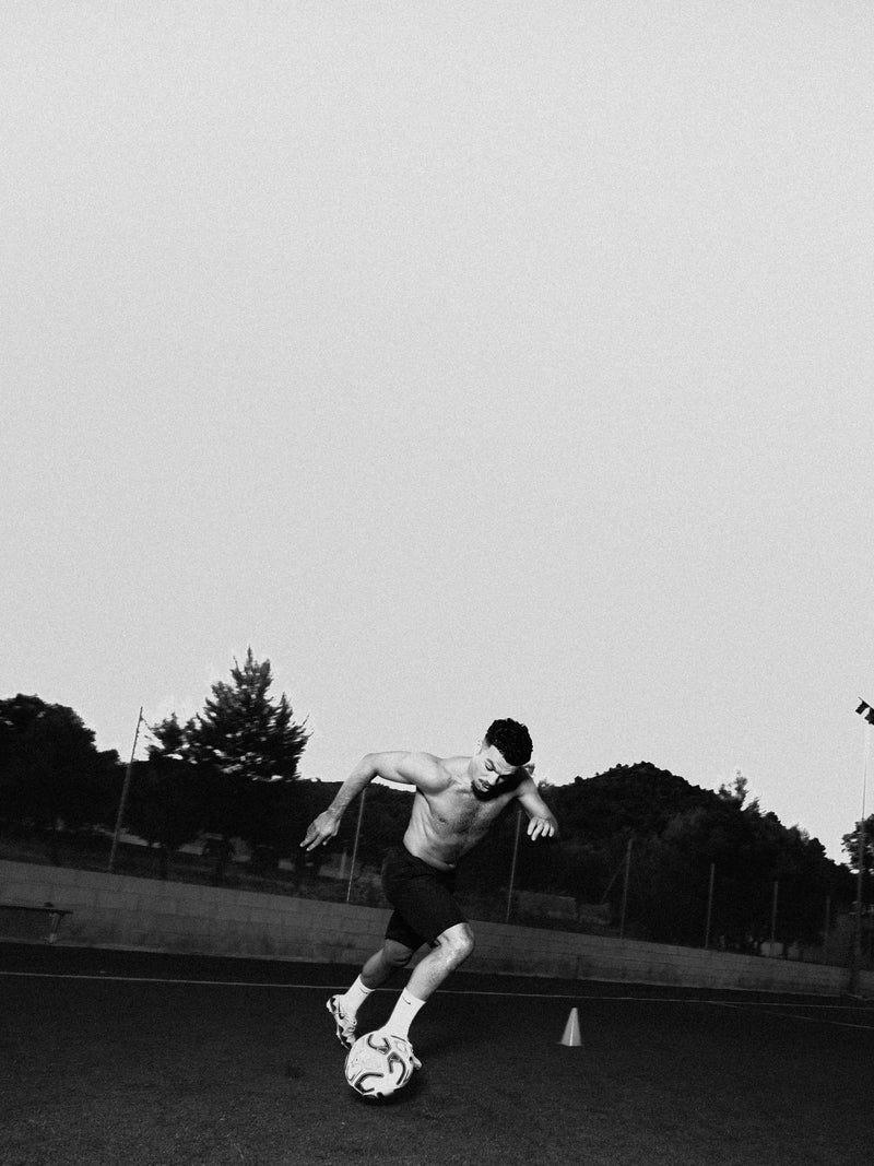 Black and white frame of a player dribbling on a training pitch