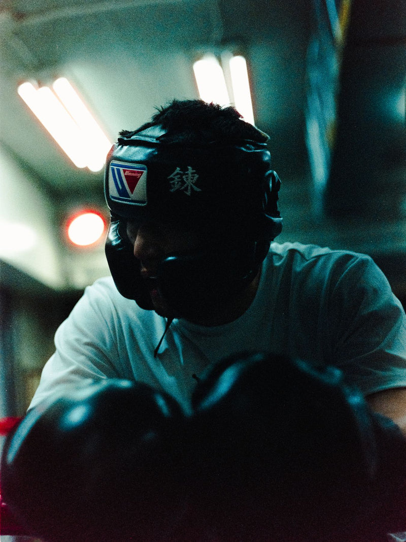 Boxer in headgear under fluorescent light, gloves raised