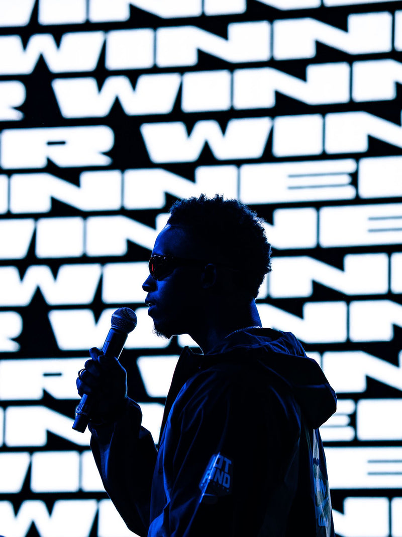 Silhouette of a host with a microphone against a lit WINNER wall